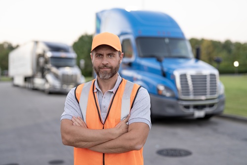 Semi-Truck Driver Standing Near 18-Wheeler Memphis TN truck driver in safety vest and cap standing arms crossed before semi-trucks