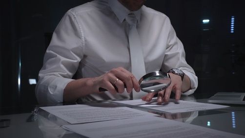 Attorney Examining Misleading Statements Securities Fraud Newton Square professional examining printed legal document closely using magnifying glass at desk