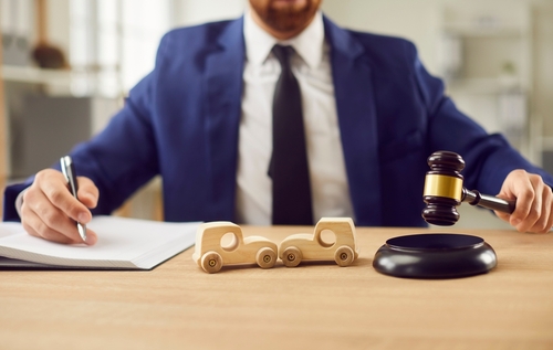 Philadelphia Commercial Auto Accident Lawyer With Gavel suited attorney holding gavel beside wooden toy car collision on desk