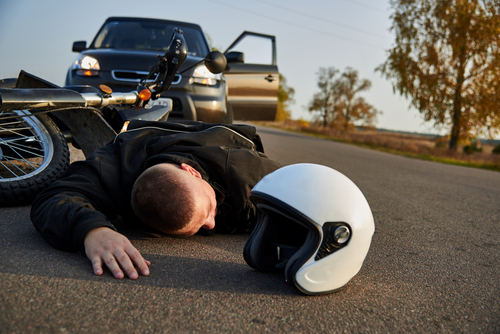 Injured Motorcyclist on Road After Crash Morgantown WV motorcyclist lying on asphalt beside fallen motorcycle and helmet after collision with SUV