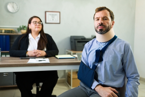 injured man wearing neck brace and arm sling seated in office consultation