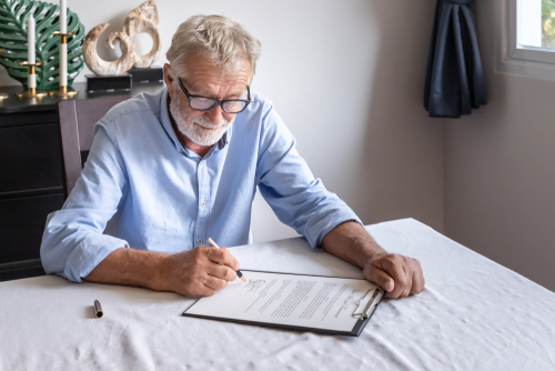 Elderly Man Signing Probate Documents Brooklyn Estate Attorney elderly man wearing glasses signing legal document on clipboard at table
