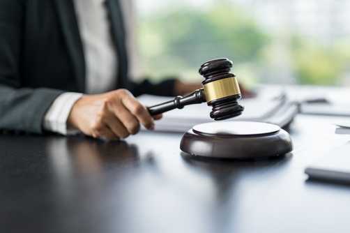 suited professional striking gavel on sound block at desk with documents