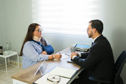 injured woman wearing arm sling meeting with suited attorney at office desk