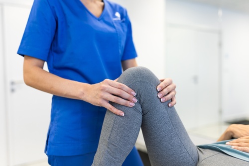 female physical therapist in scrubs examining patient knee during clinical evaluation