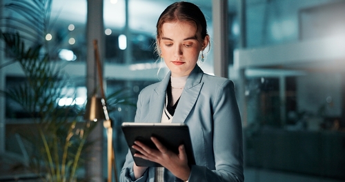 1099 Worker Reviewing Overtime Misclassification Rights on Tablet professional woman in blazer reviewing documents on tablet in office at night