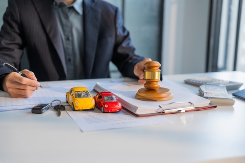 Roanoke Car Accident Lawyer Reviewing Contributory Negligence Claim attorney writing on legal documents beside gavel and toy car collision models
