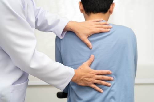 Atlanta Workers Comp Doctor Examining Back Injury Patient physical therapist in white coat examining patient's back and shoulder