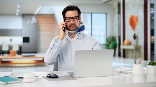 Injured Man Calling Cruise Accident Attorney in Plantation Florida man wearing neck brace talking on phone while working at laptop