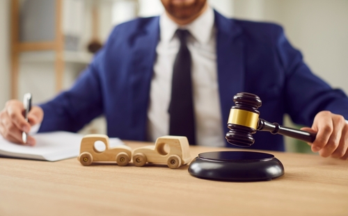 Fort Lauderdale Car Accident Attorney Gavel Comparative Negligence suited lawyer holding gavel beside wooden toy cars on desk while writing