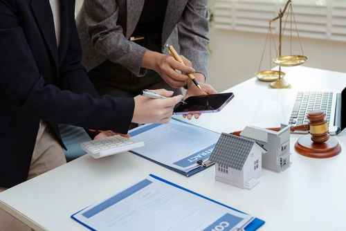 two professionals reviewing contract documents beside gavel, scales of justice, and house model