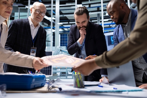 business professionals with ID badges reviewing documents at industrial facility meeting