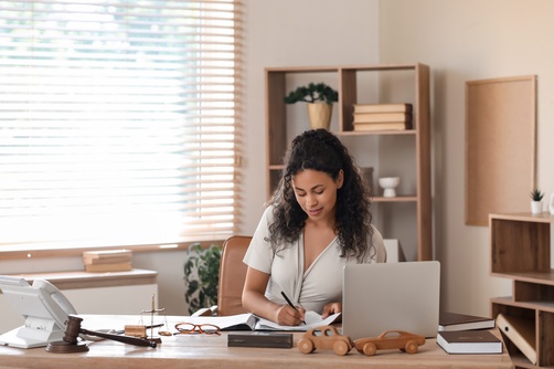 Roanoke Car Accident Lawyer Reviewing Auto Accident Claim Female attorney writing notes at desk with gavel, scales, and laptop