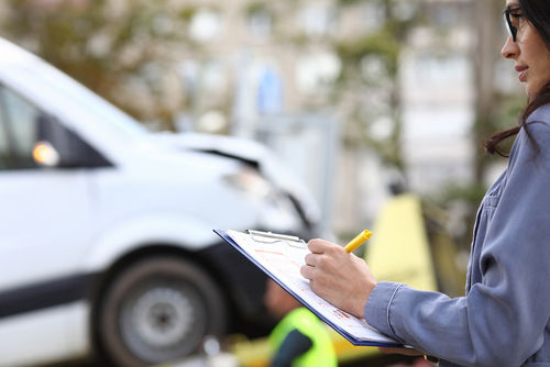 insurance agent filling out paperwork on clipboard at vehicle accident scene