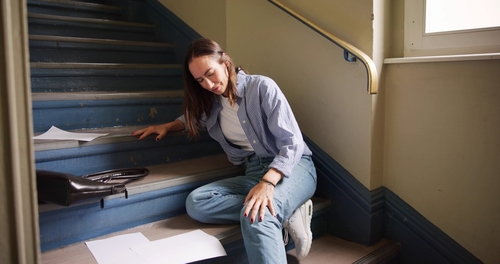 woman sitting on staircase holding knee after apparent slip and fall