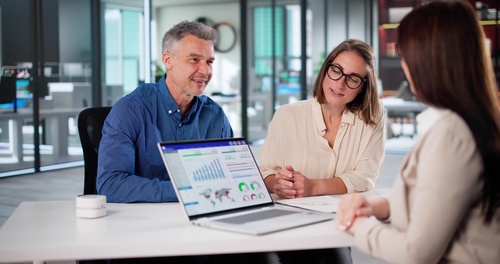 couple meeting with advisor reviewing financial charts on open laptop