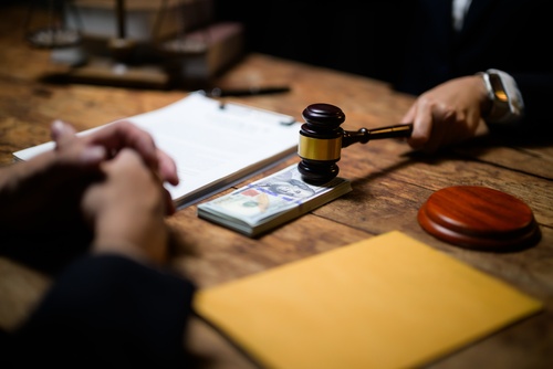 hand holding judge gavel over cash and legal documents on wooden desk