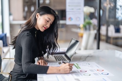 USA Securities Fraud Lawyer Reviewing Rule 10b-5 Investor Claims businesswoman reviewing printed reports and charts while working on laptop at desk