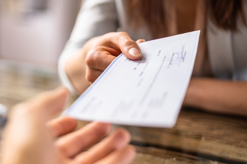 employee receiving payroll cheque handed over wooden desk during payment