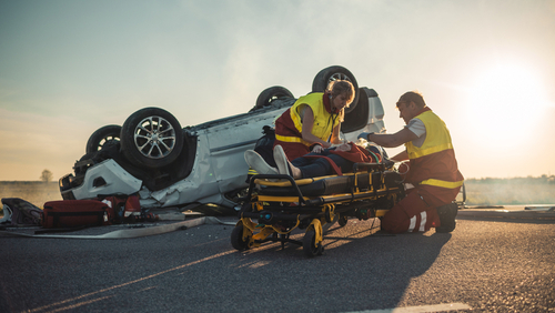 two paramedics treating injured victim on stretcher beside overturned vehicle at crash scene