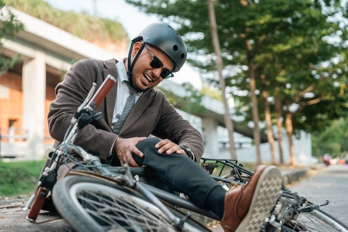 suited man wearing helmet clutching knee after falling from bicycle outdoors