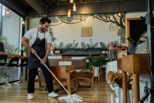 male worker wearing apron mopping hardwood floor inside cafe restaurant