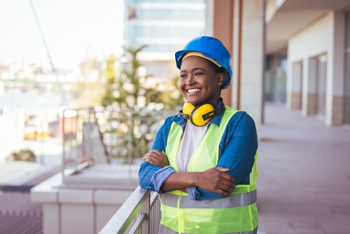 Manhattan City Construction Worker On Job Site confident female construction worker wearing hard hat, ear protection, and safety vest