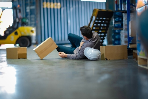 Staten Island City Worker Injured on the Job warehouse worker fallen on floor clutching shoulder beside scattered cardboard boxes