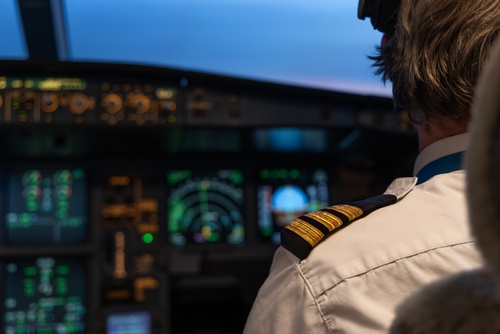 Pilot In Cockpit Facing FAA Medical Deferral pilot in uniform with gold epaulettes seated in illuminated airplane cockpit