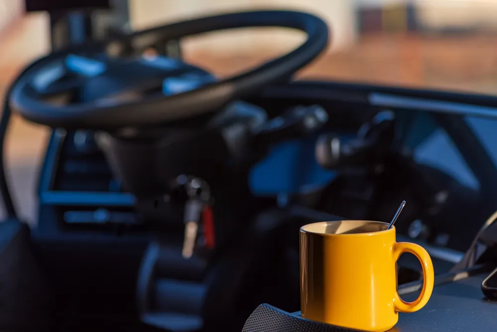 Coffee mug with spoon beside truck steering wheel and ignition keys