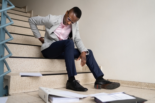 Man sitting at the bottom of a staircase holding his back from slipping down the steps