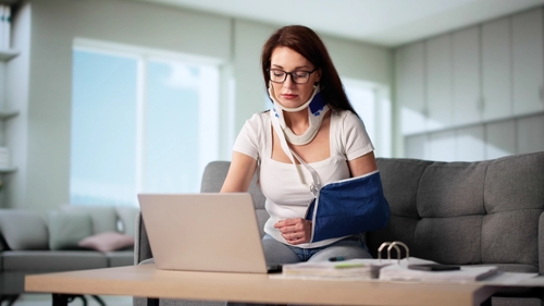 Woman wearing a neck brace and arm sling typing on a laptop